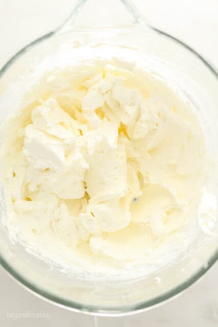 A glass mixing bowl with whipped cream cheese frosting