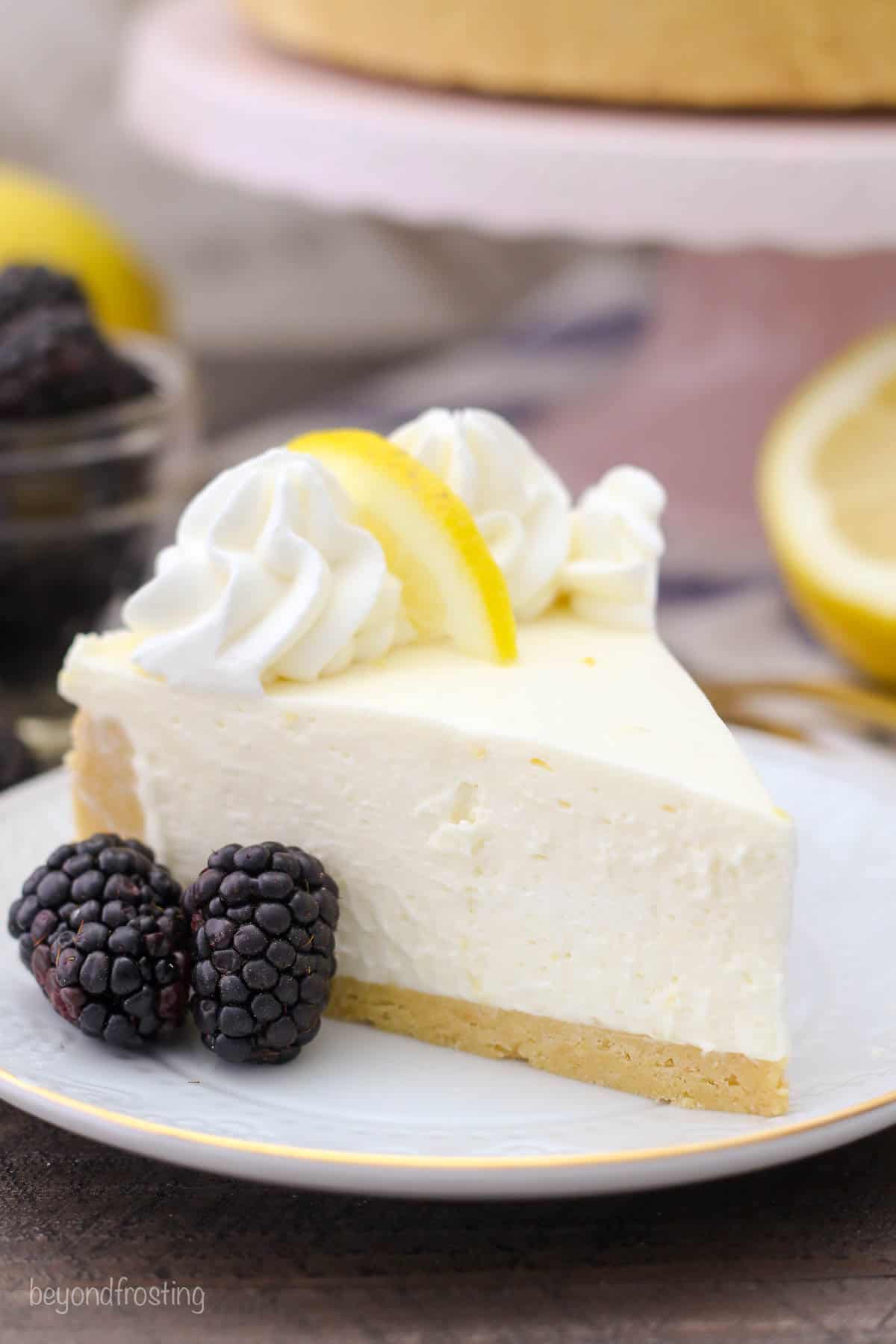 side view of a slice of lemon cheesecake on a white plate with two blackberries