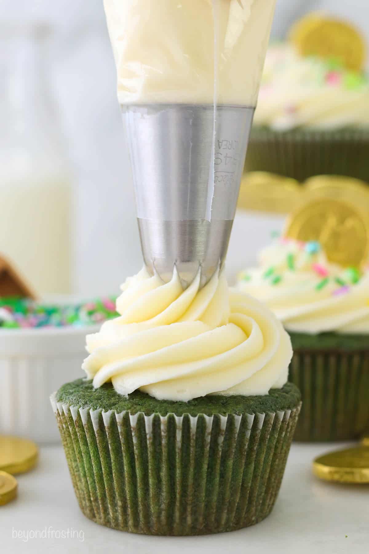 A piping bag frosting a green cupcake with cream cheese frosting