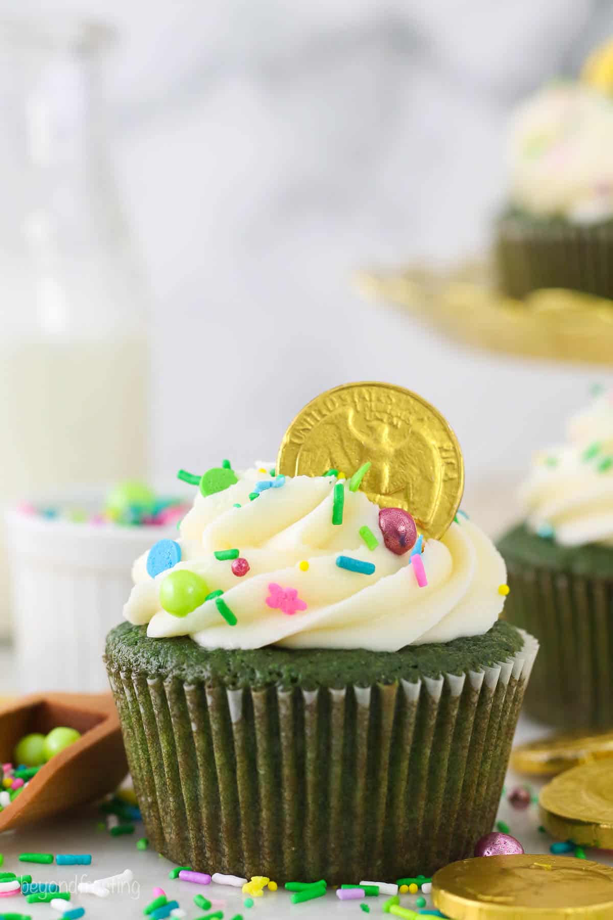A green cupcake decorated for St. Patrick's Day with sprinkles and a gold coin