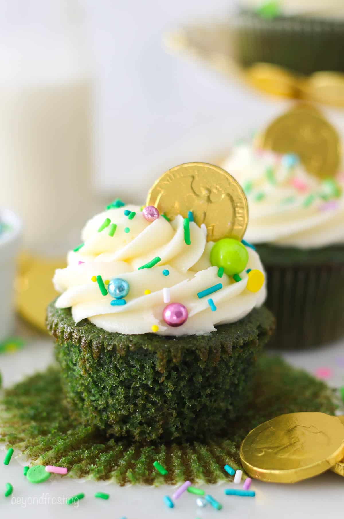 An unwrapped green cupcake topped with sprinkles and a chocolate gold coin