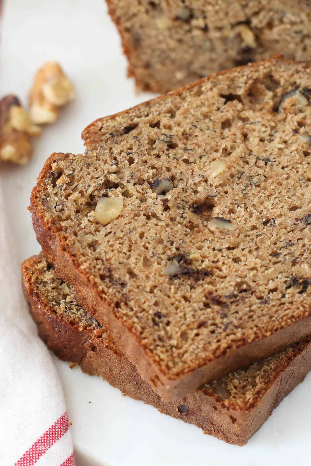 Close up of two slices of whole wheat banana bread stacked on a white countertop.