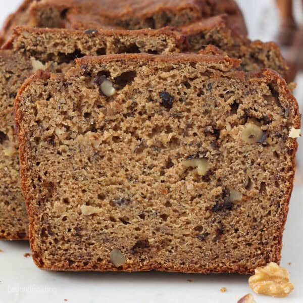 Close up front view of a slice of whole wheat banana bread leaning against the rest of the loaf.