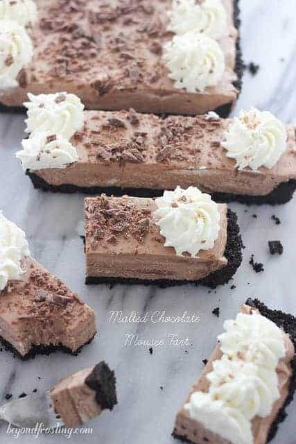 A bunch of pieces of a malted chocolate mousse tart with swirls of homemade whipped cream on top