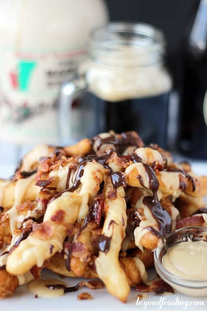 A pile of freshly-made bacon maple donut fries with a bottle of maple syrup behind them