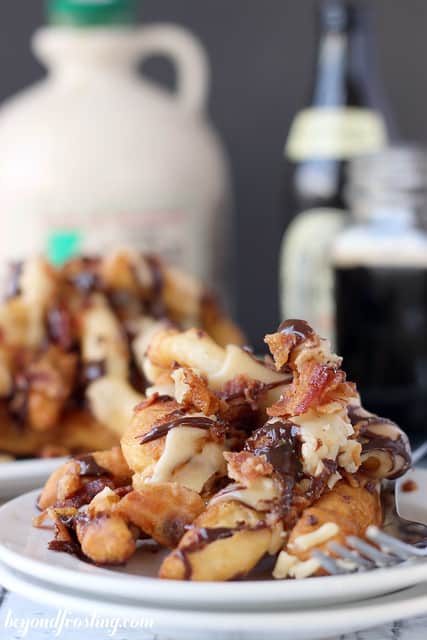 Two stacked plates holding a pile of donut fries topped with bacon bits, maple glaze and hot fudge sauce