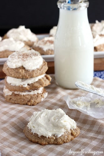 Frosted sugar cookies on a dining room table with an offset spatula and a glass of milk