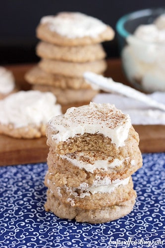 A stack of four maple walnut sugar cookies on a blue and white tablecloth in front of another stack of cookies on a cutting board
