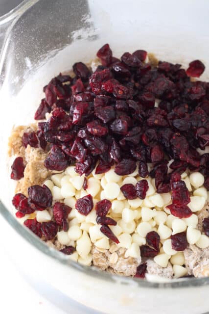 Dried cranberries and white chocolate chips added to oatmeal cookie dough in a bowl