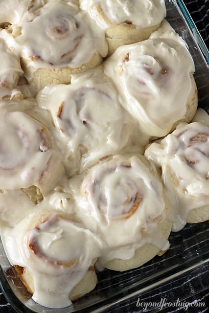A glass baking dish full of homemade cinnamon rolls topped with a generous amount of icing