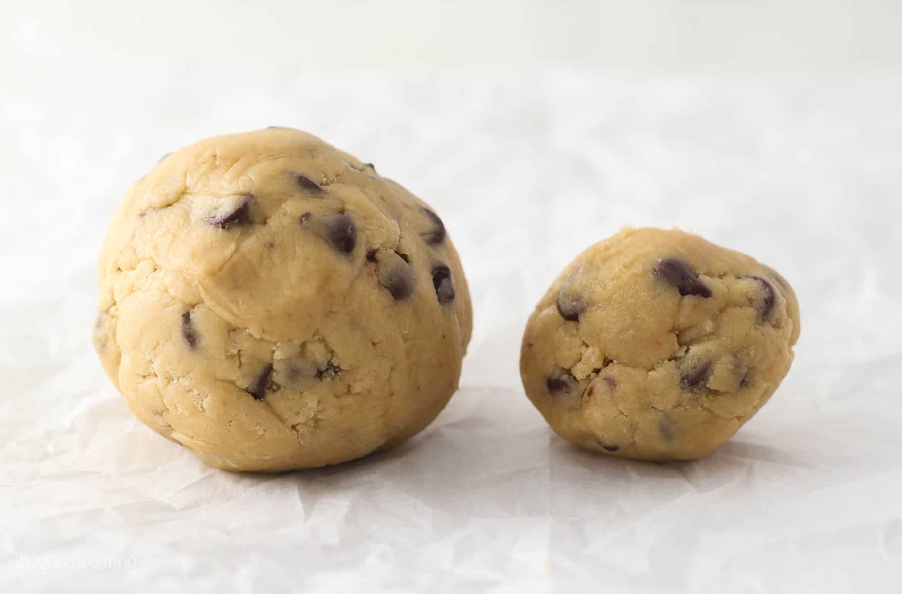 A large ball of cookie dough next to a regular sized ball of cookie dough