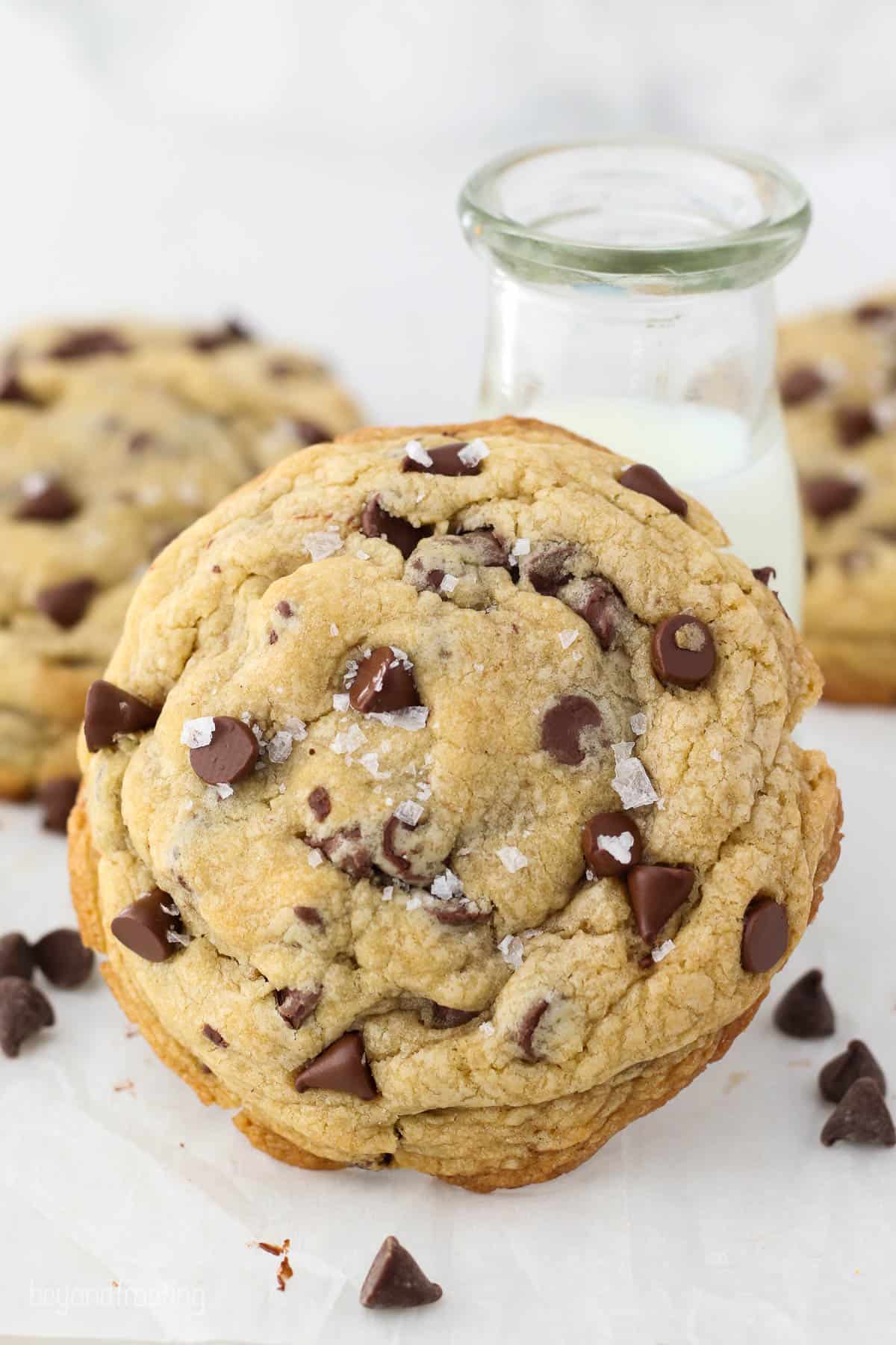 A giant chocolate chip cookie leaning against a jar of milk