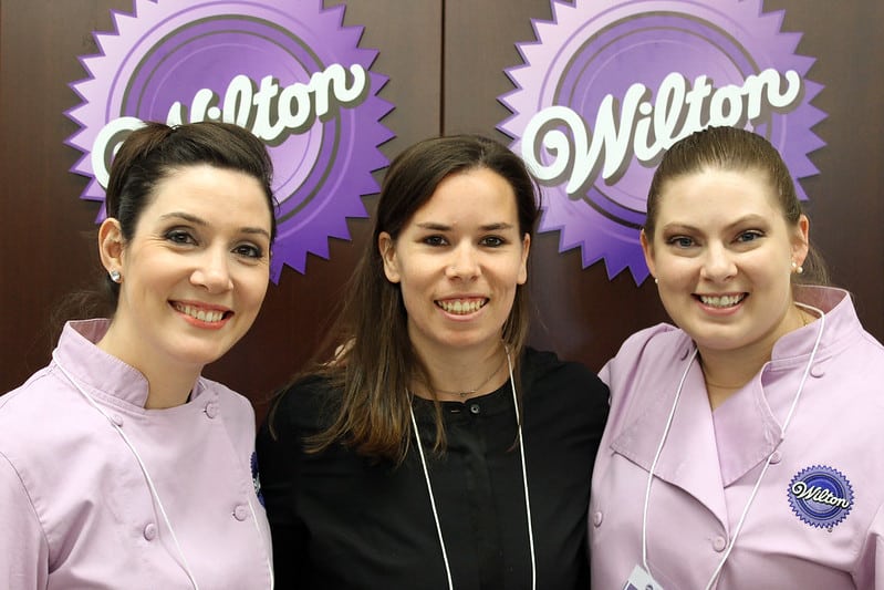 Author posing with two cake artists in front of a Wilton sign