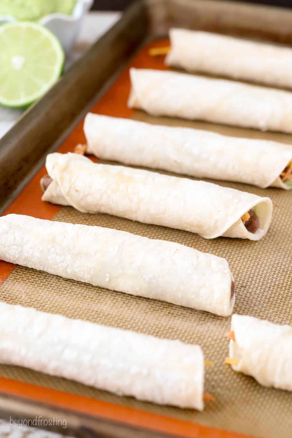 rolled, unbaked taquitos lined on a baking sheet