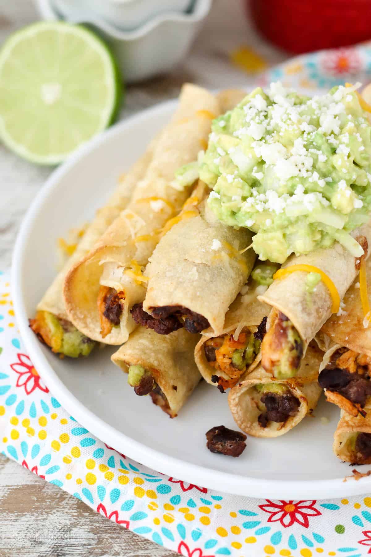 overhead of a pile of chicken taquitos on a plate topped with tomatillo avocado salsa