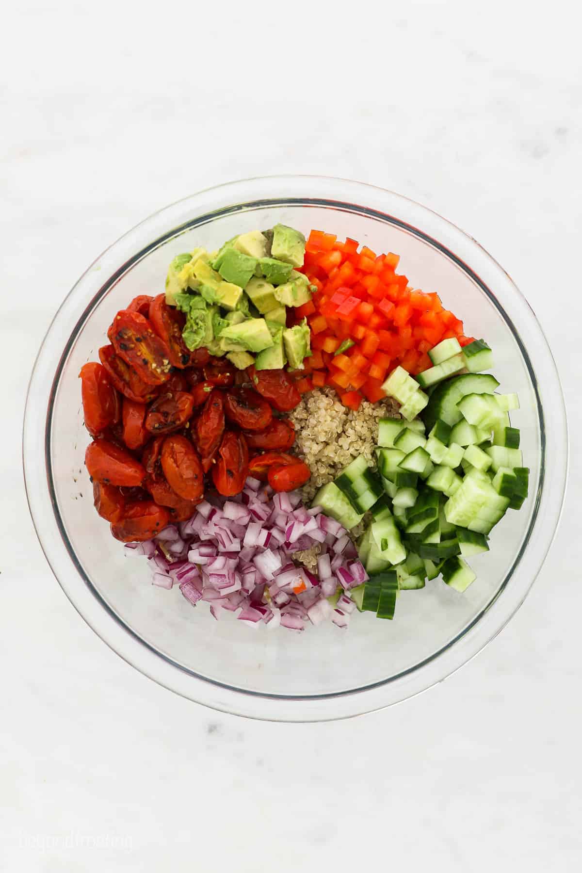 a clear glass bowl with chopped avocado, red pepper, cucumber, onion and roasted tomatoes