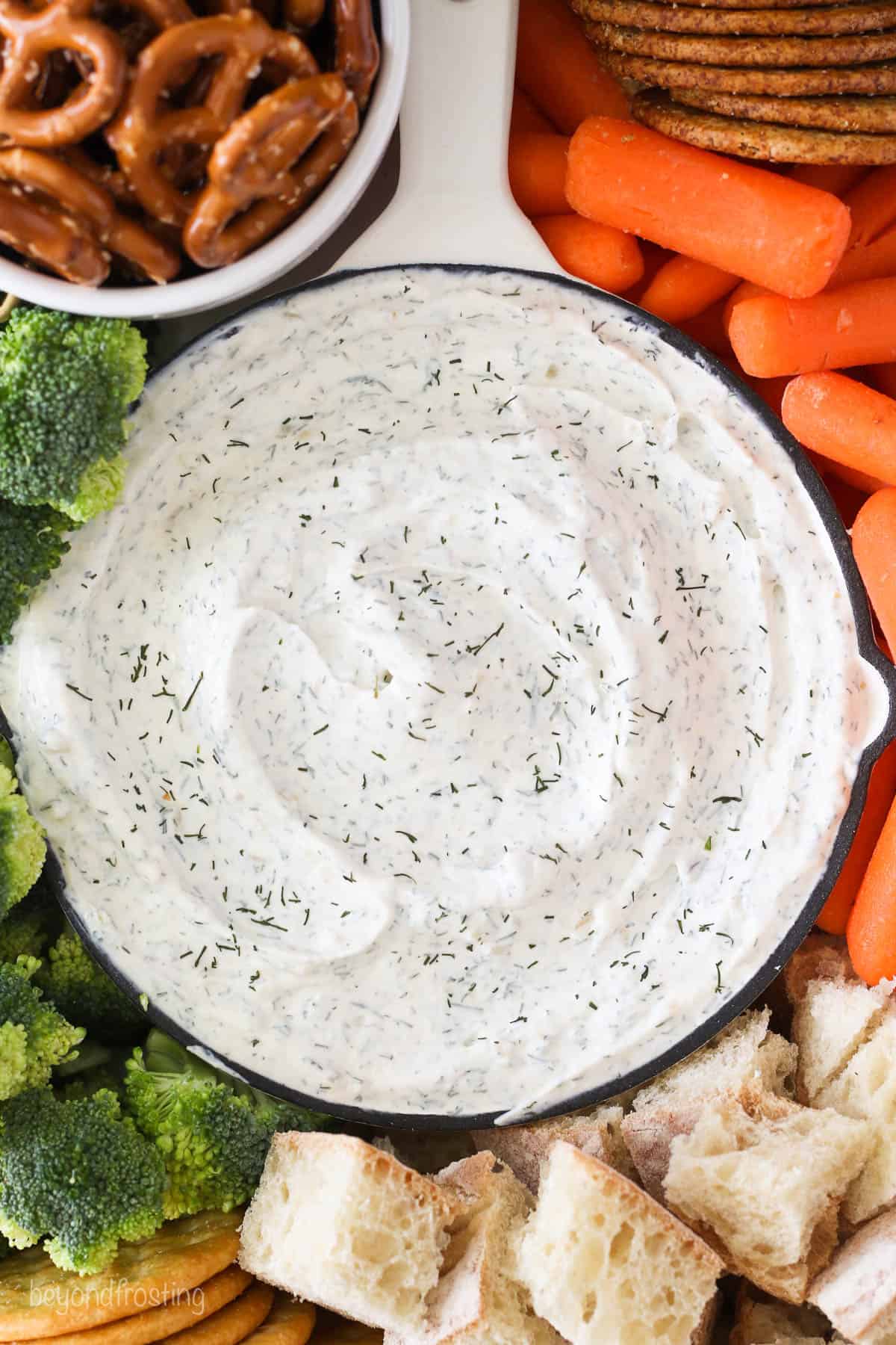 Overhead view of a bowl of dill dip next to veggies and bread