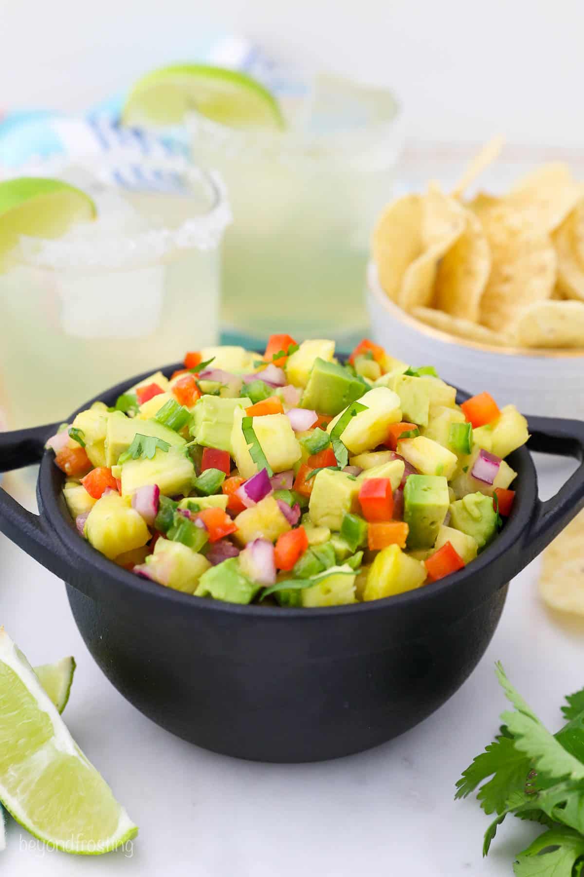 bowl of pineapple salsa in front of two margaritas and a bowl of chips