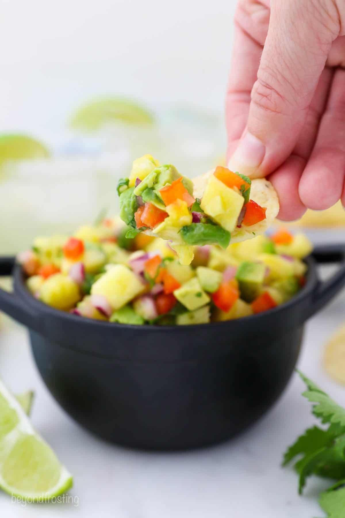 tortilla chip dipped in pineapple salsa held over a bowl