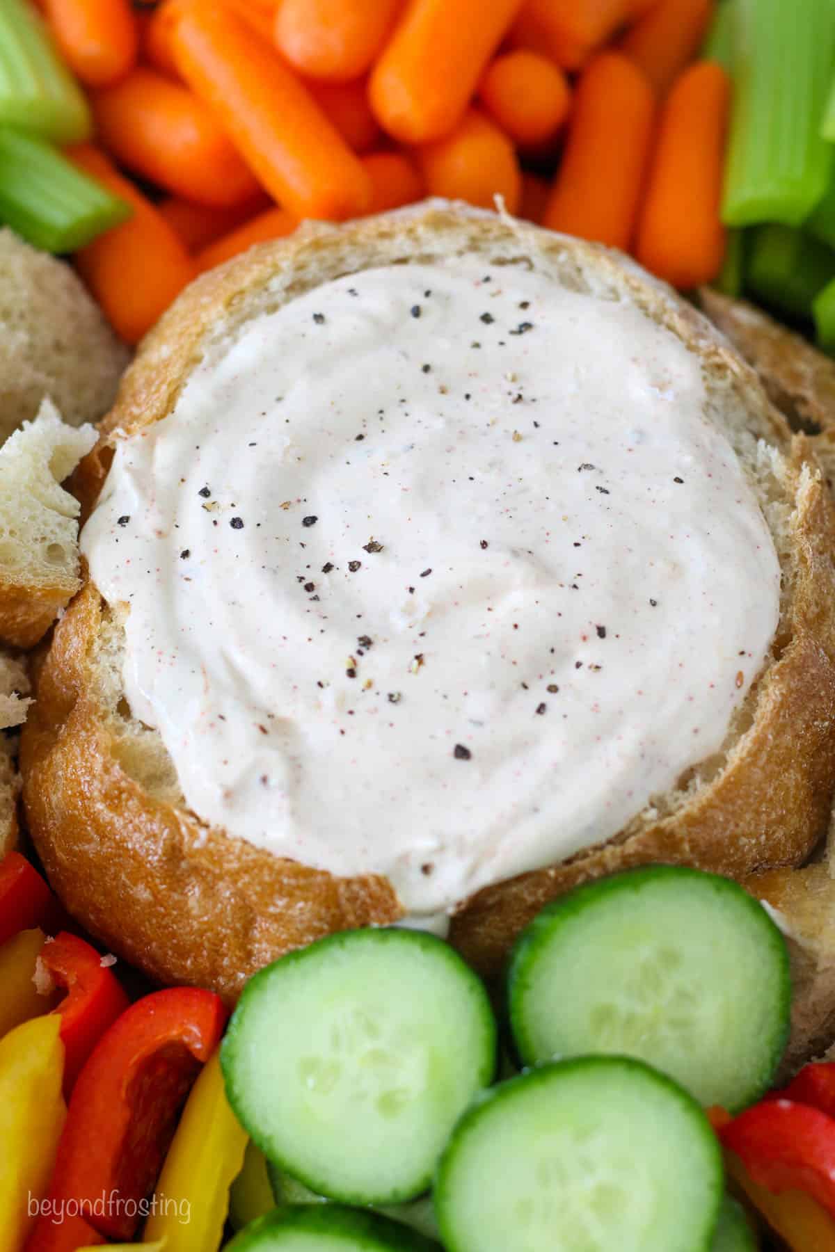Vegetable dip in a bread bowl surrounded by veggies