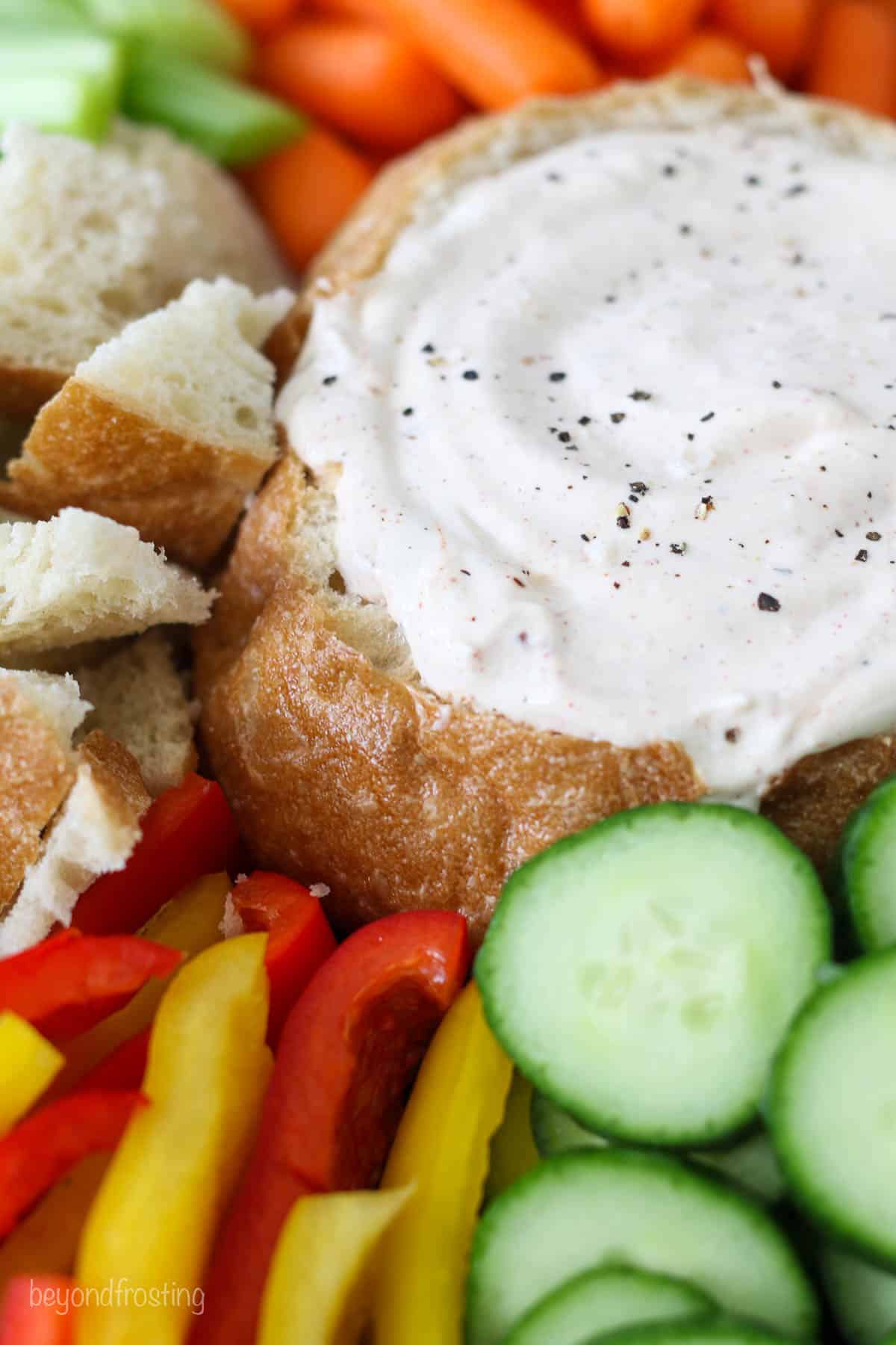 Overhead view of a bread bowl with veggie dip surrounded by veggies