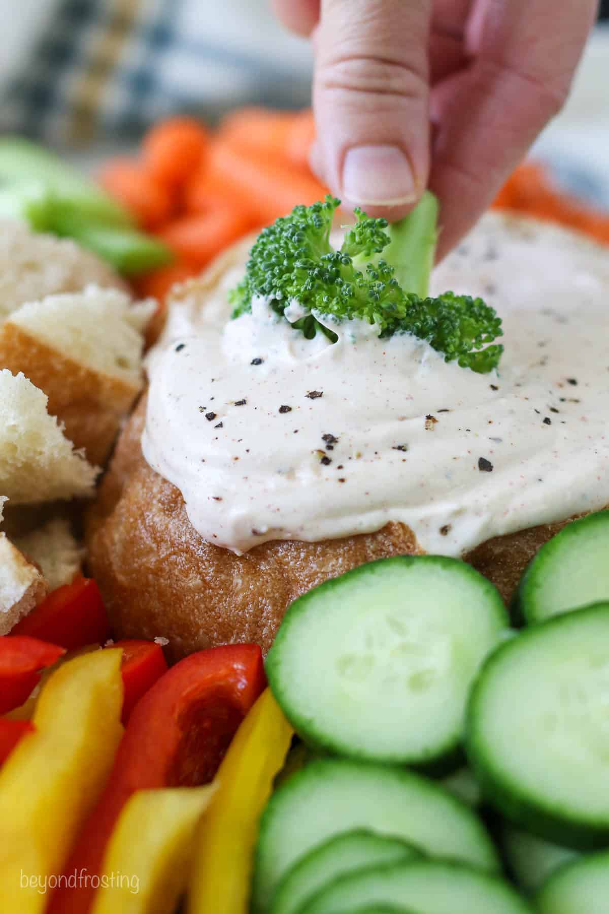 A hand dipping broccoli into veggie dip