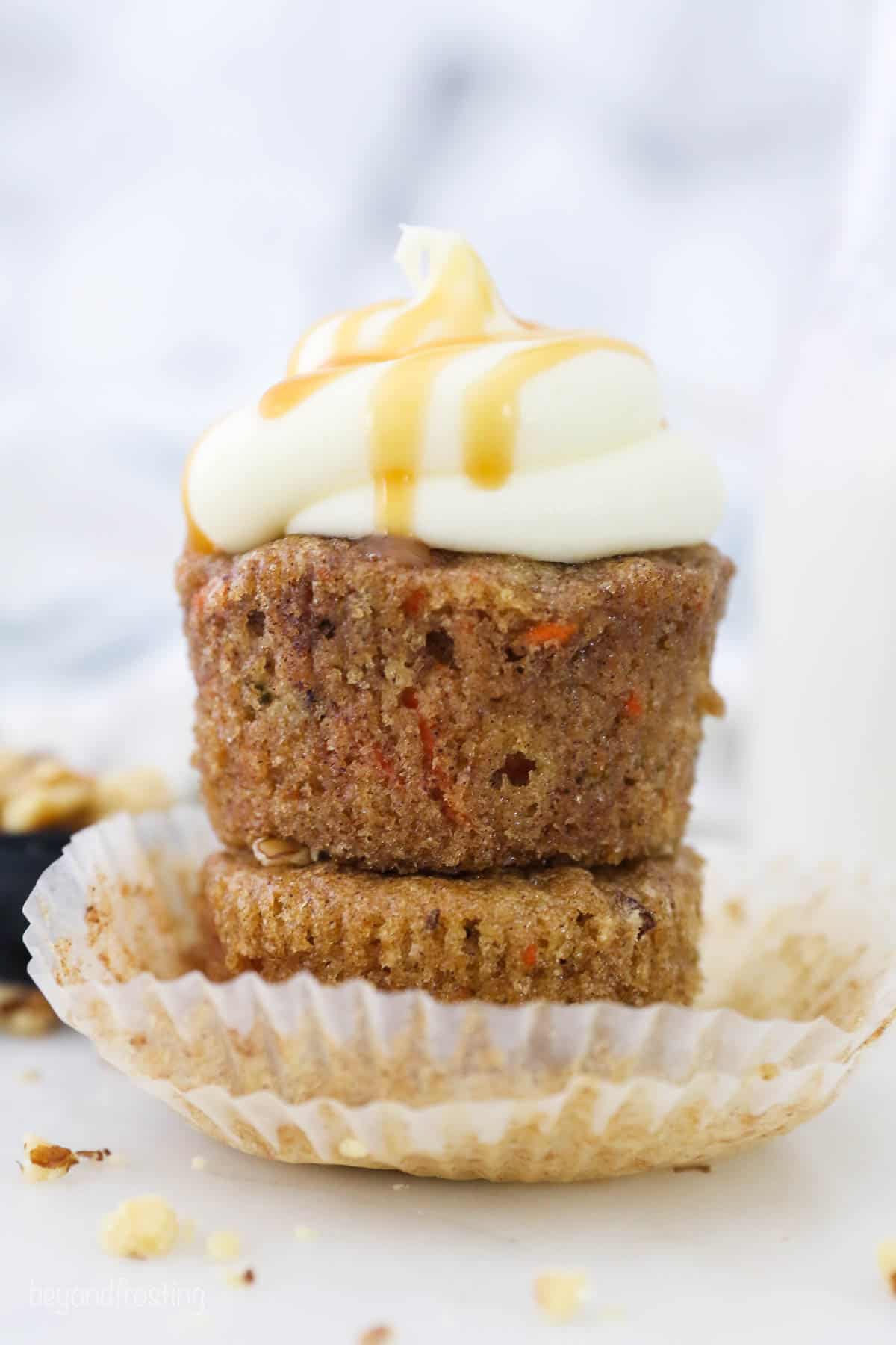 Two gluten free carrot cake cupcakes stacked on each other, the top with cream cheese frosting