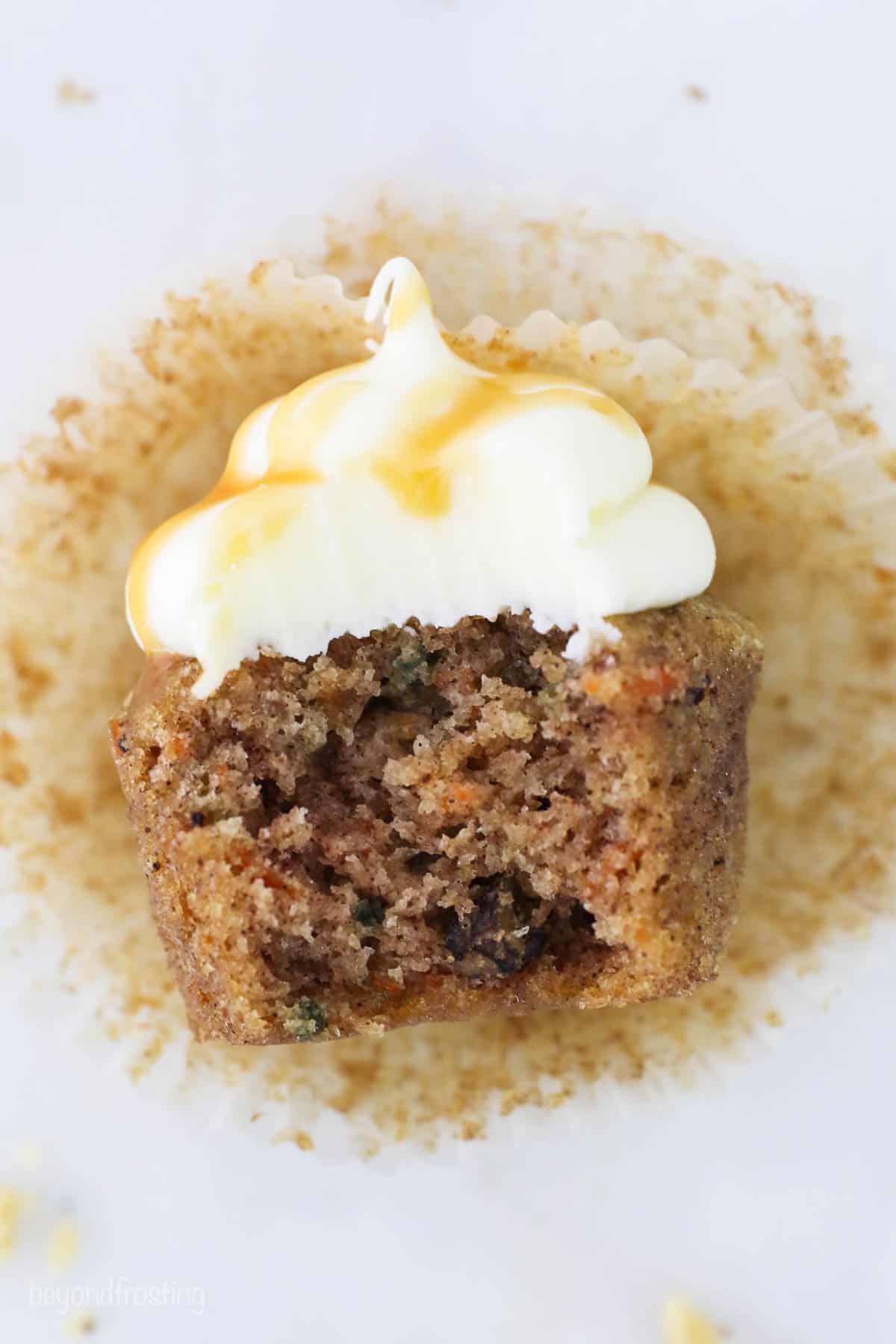 A carrot cake cupcake laying on its side with a bite missing