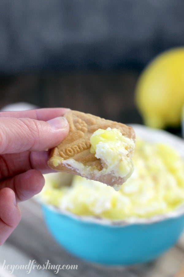 cookie dipped in cheesecake dip held over a bowl of dip