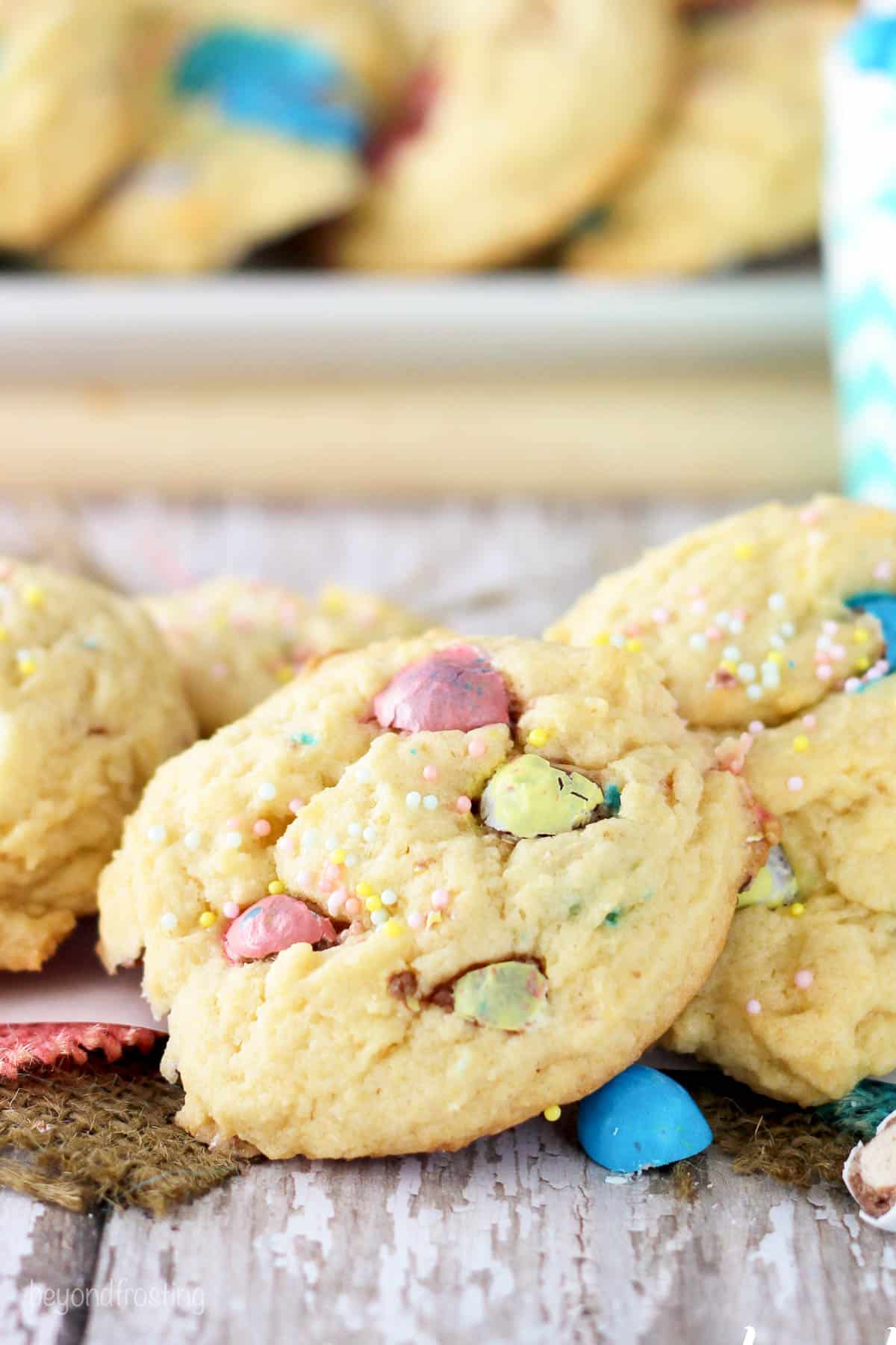 Malted cheesecake cookies piled onto a dining table with a platter holding more cookies in the background