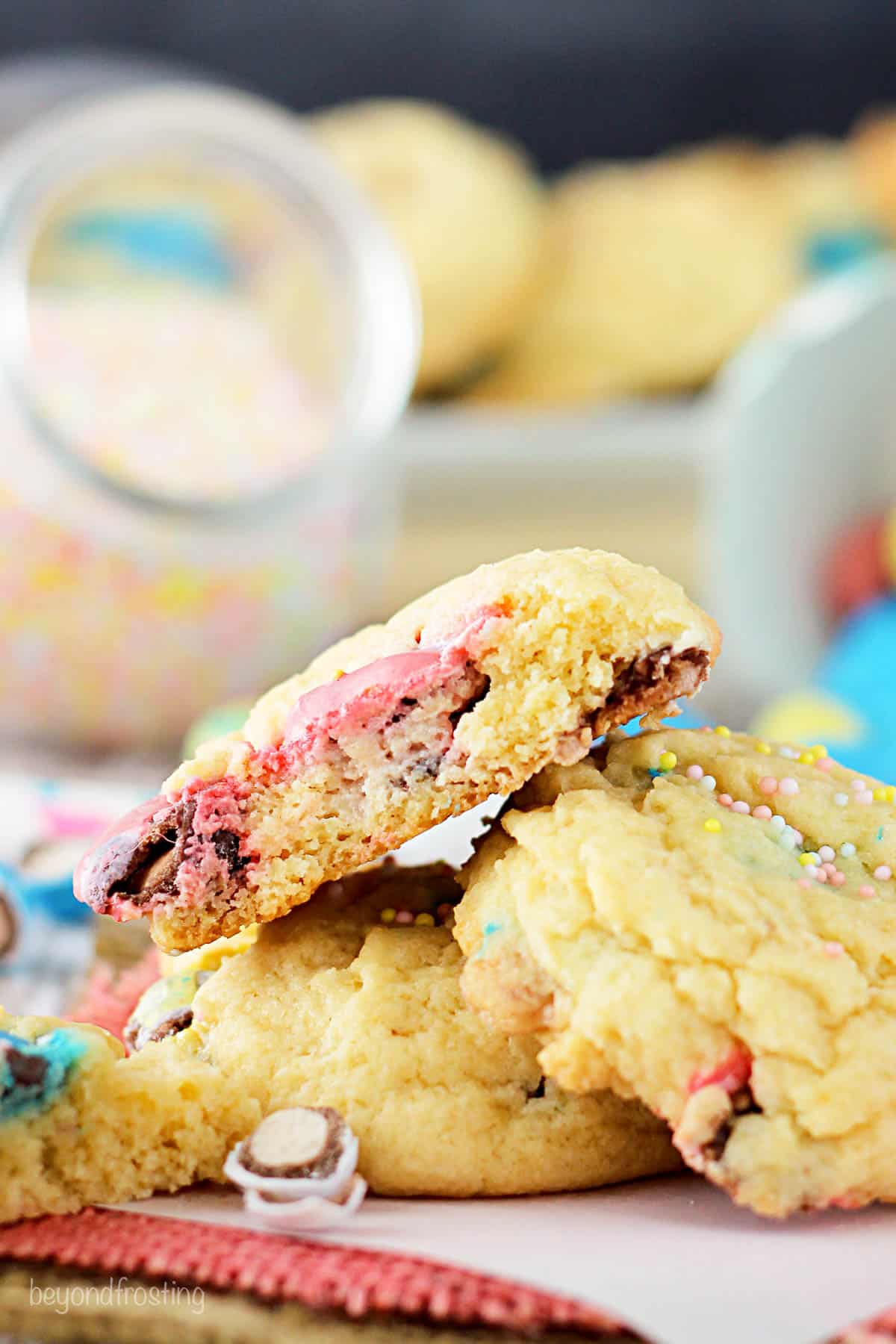 Three malted cheesecake cookies stacked on top of each other with more cookies and candies in the background