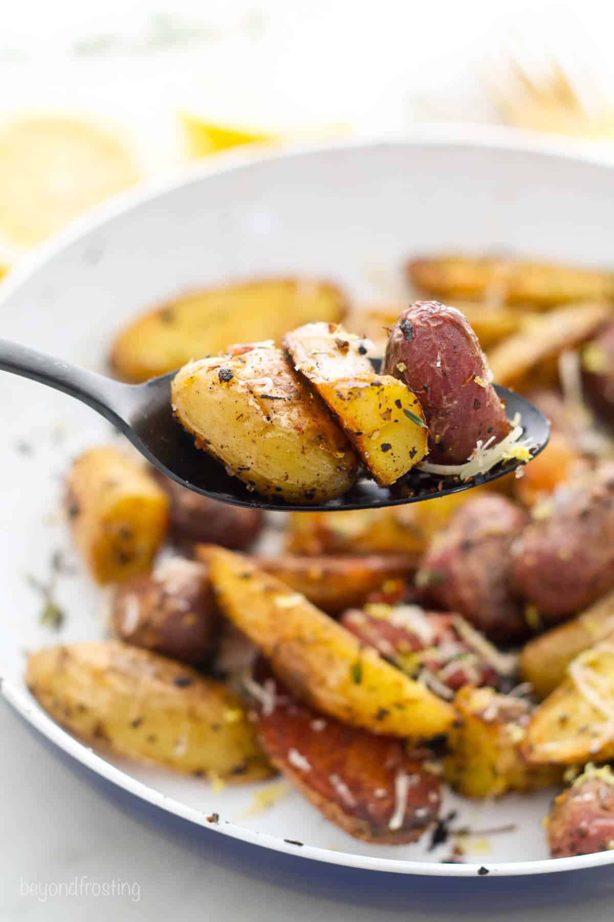 three pieces of lemon potatoes on a spoon held above a plate with more potatoes