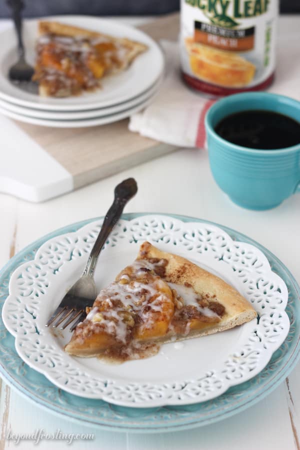 a slice of peach pizza on a plate with a fork with coffee and another slice of pizza in the background