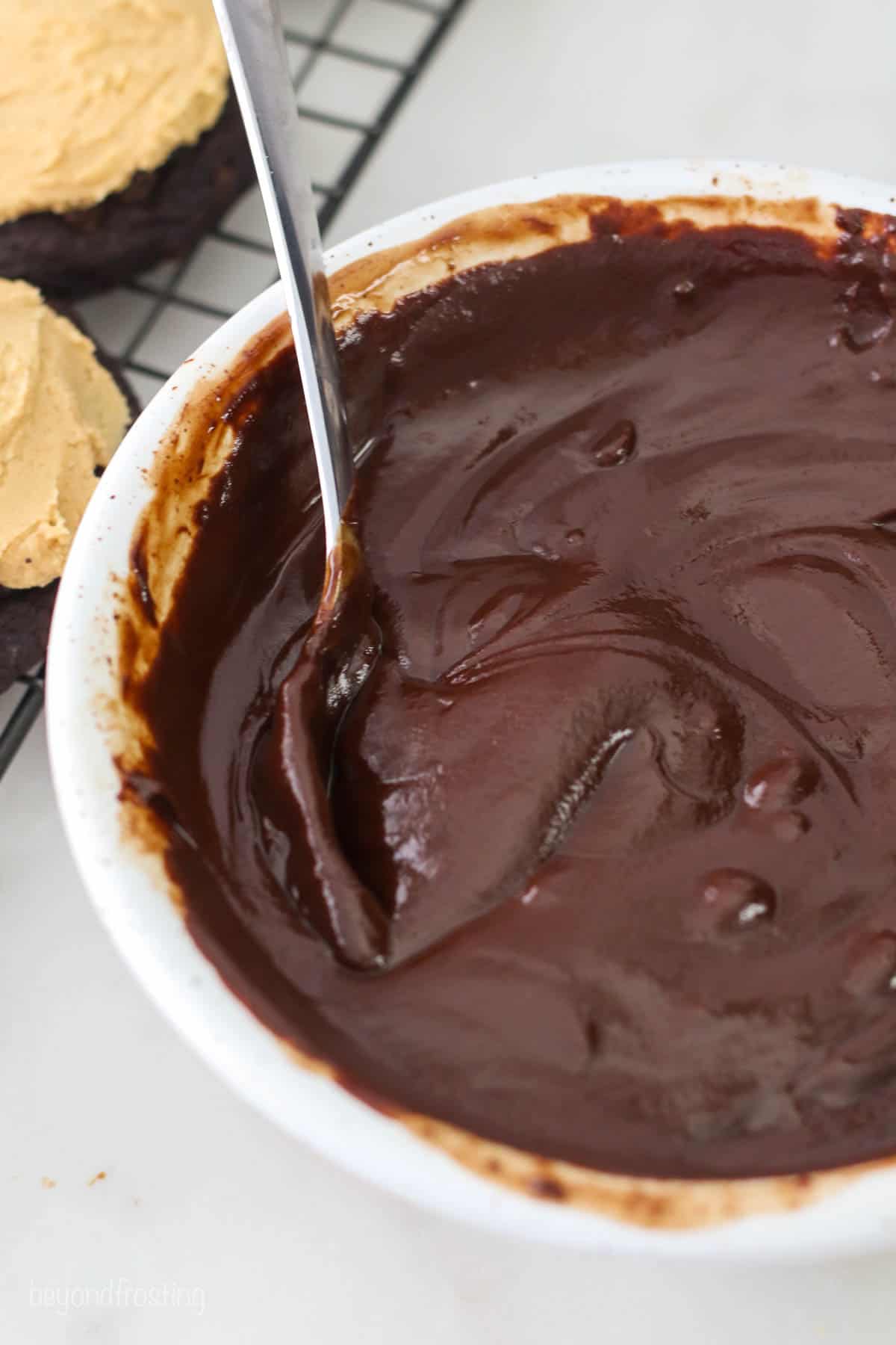 A metal spoon stirring chocolate ganache in a white bowl