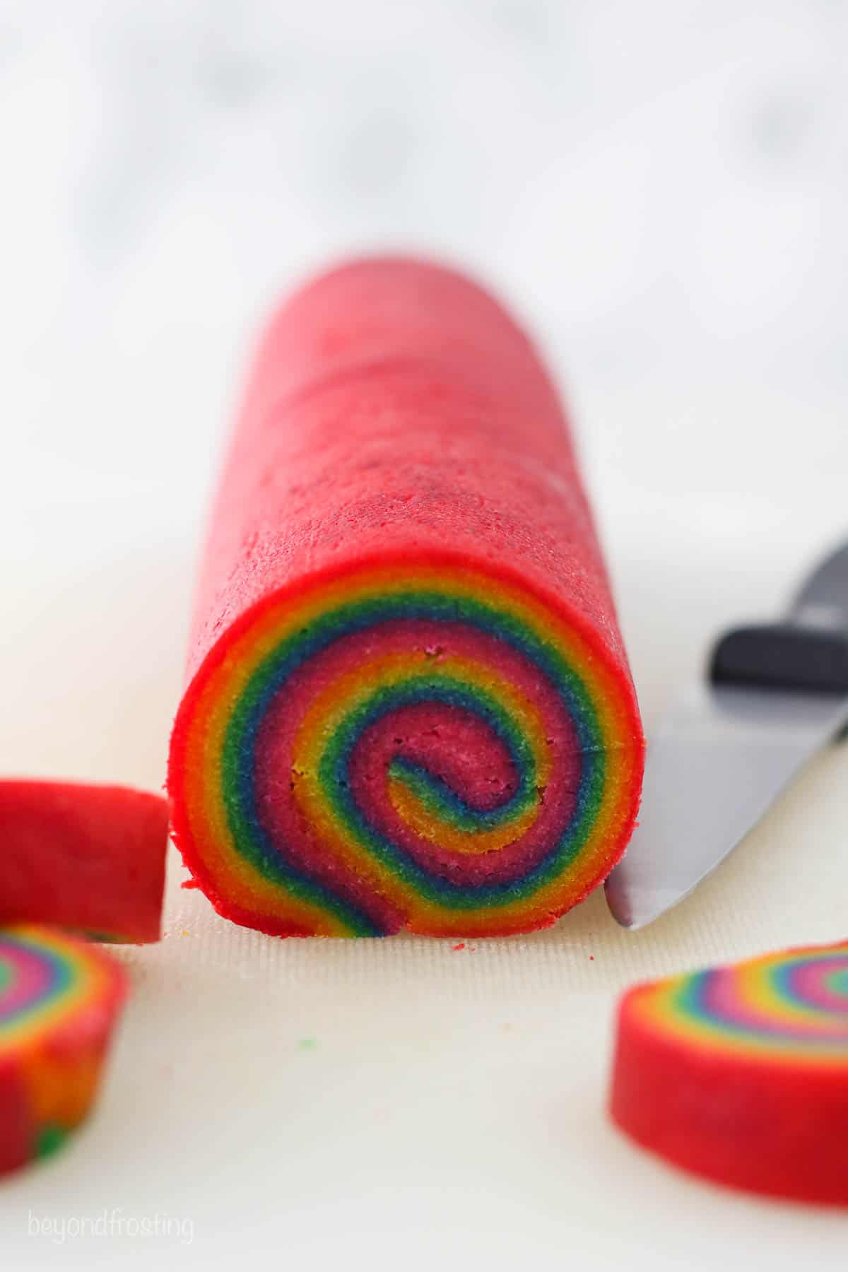 A log of rainbow swirl cookie dough next to a knife.