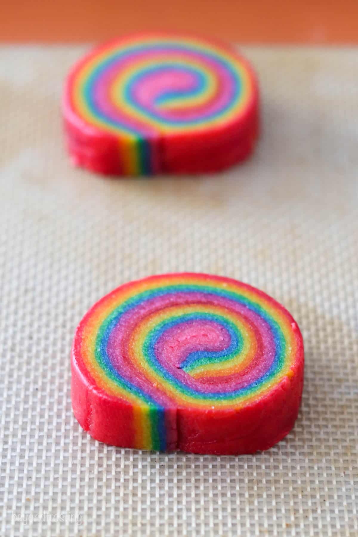 Two rainbow swirl cookies on a baking sheet.