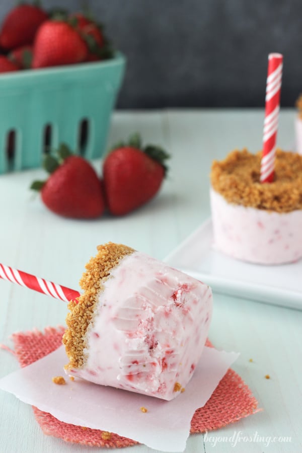 partially eaten strawberry popsicle on its side on a napkin with strawberries and popsicles in the background