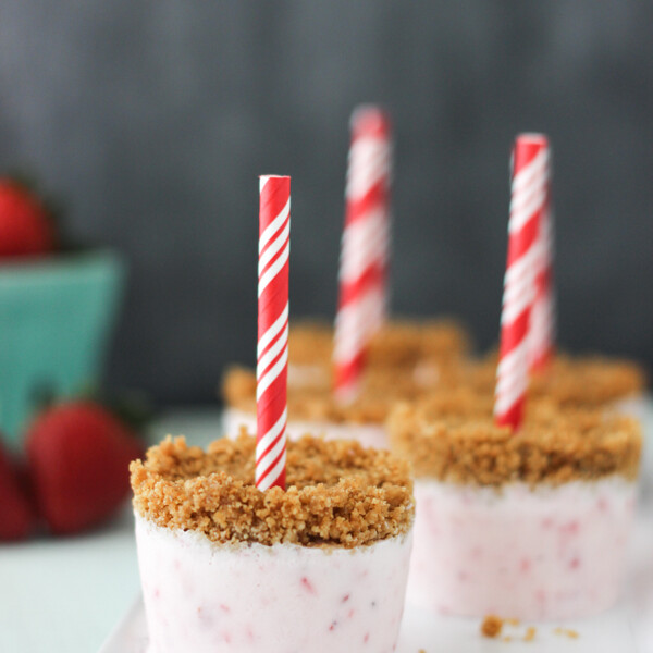 side view of strawberry popsicles standing upright on a white plate