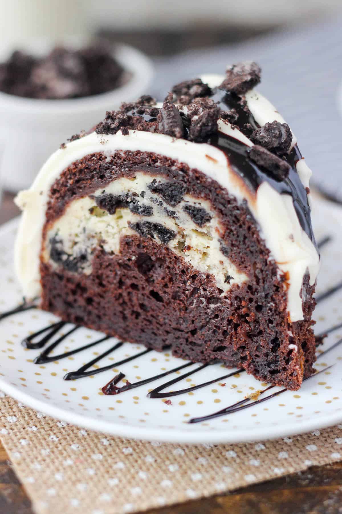 a slice of chocolate bundt cake on a white plate drizzled with hot fudge