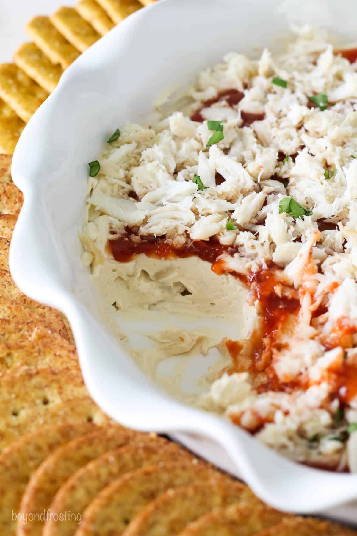 A pie dish of cold crab dip with a few servings missing