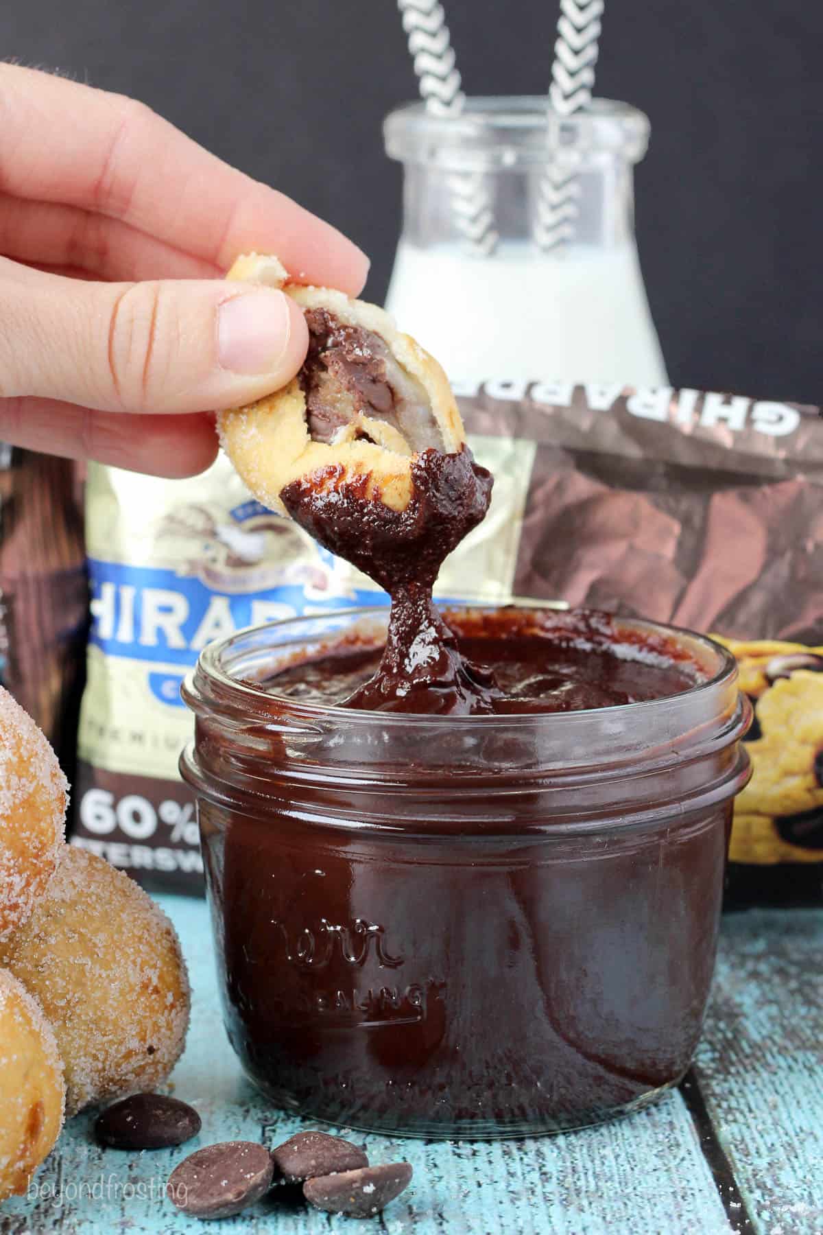 a cookie dough donut hole with a bite out being dipped into a jar of melted chocolate