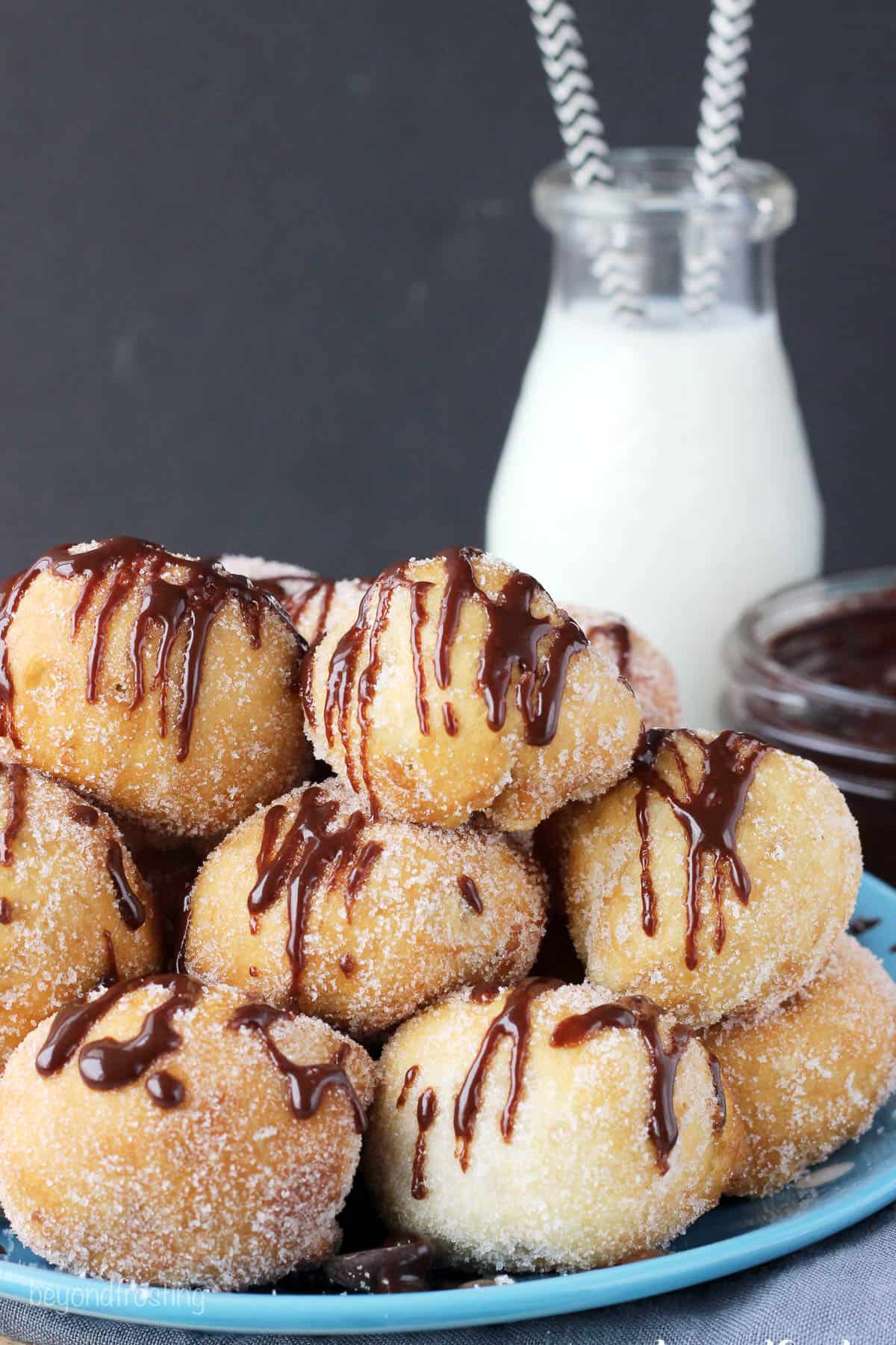 side view of a pile of cookie dough donut holes on a plate with a jug of milk in the background