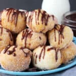 a pile of cookie dough donut holes drizzled with chocolate on a blue plate