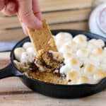 closeup of a graham cracker being dipped into a small skillet filled with s'mores dip