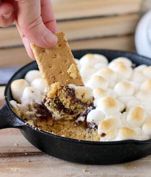 closeup of a graham cracker being dipped into a small skillet filled with s'mores dip