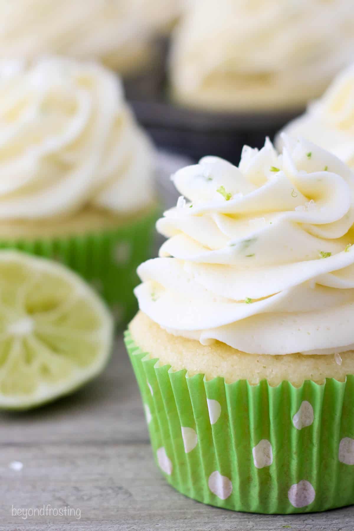 A close up of a frosted margarita cupcake in a green polka dot liner