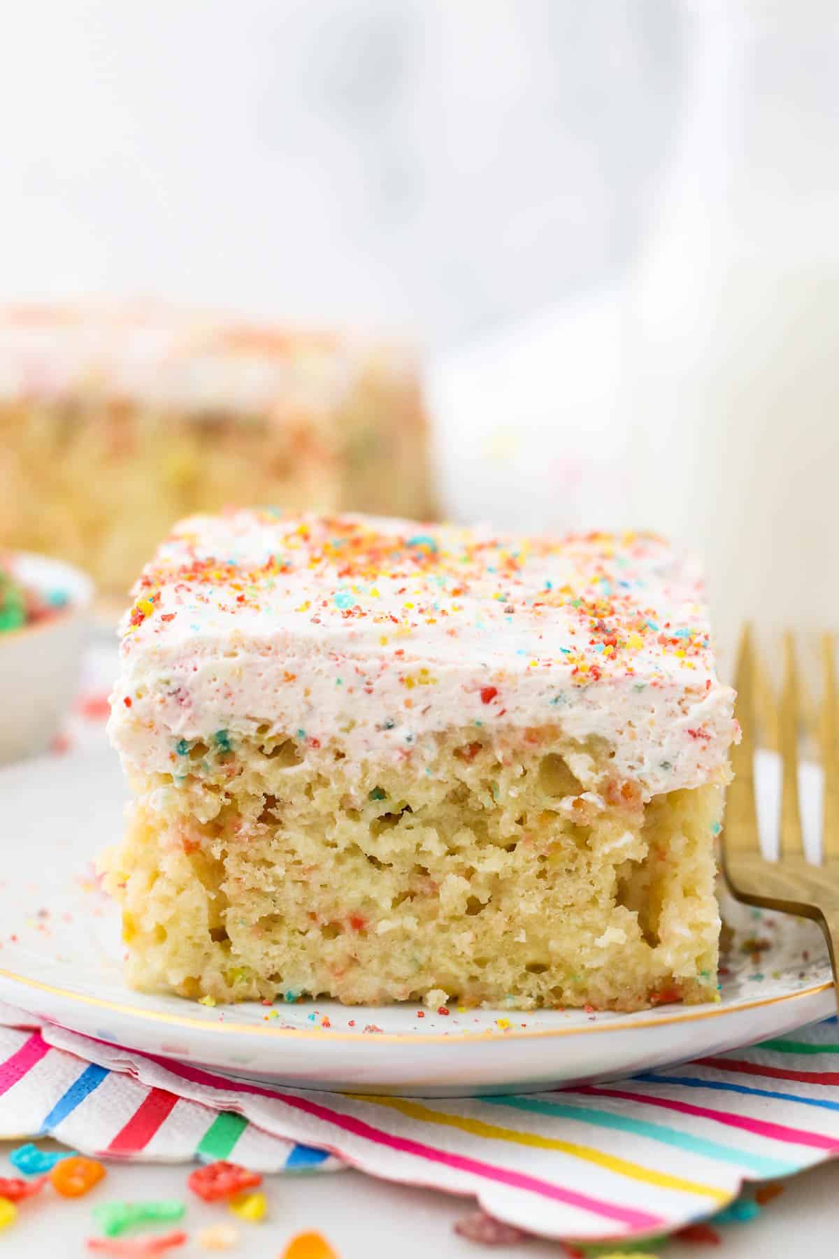 A slice of Fruity Pebble Cake with Whipped Cream on a white plate