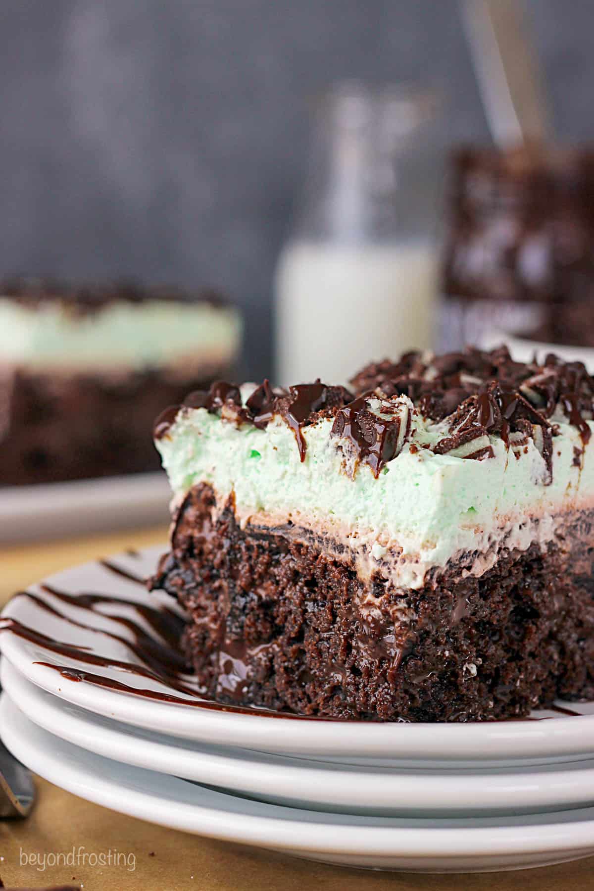 closeup of a slice of double chocolate mint poke cake on a stack of white plates