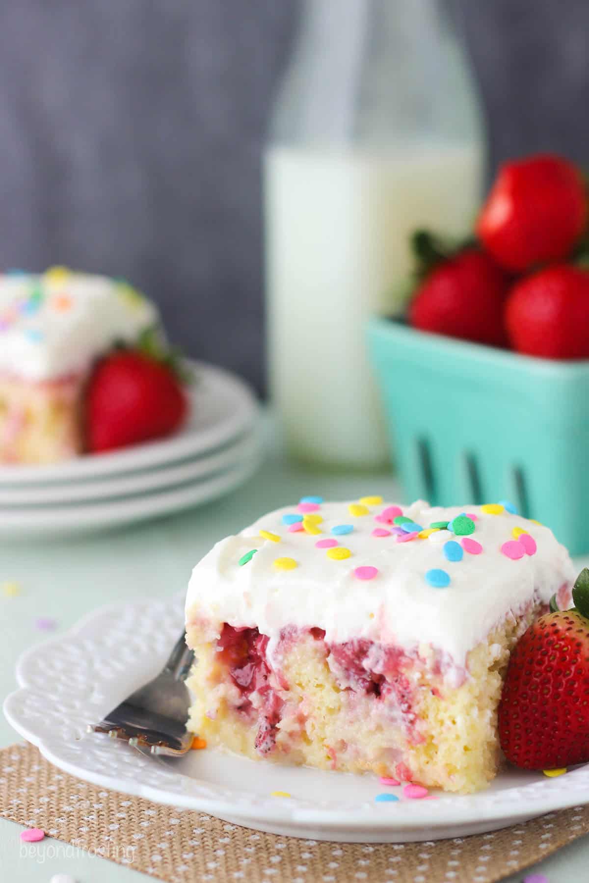 overhead of a slice of cake on a plate with milk and strawberries in the background