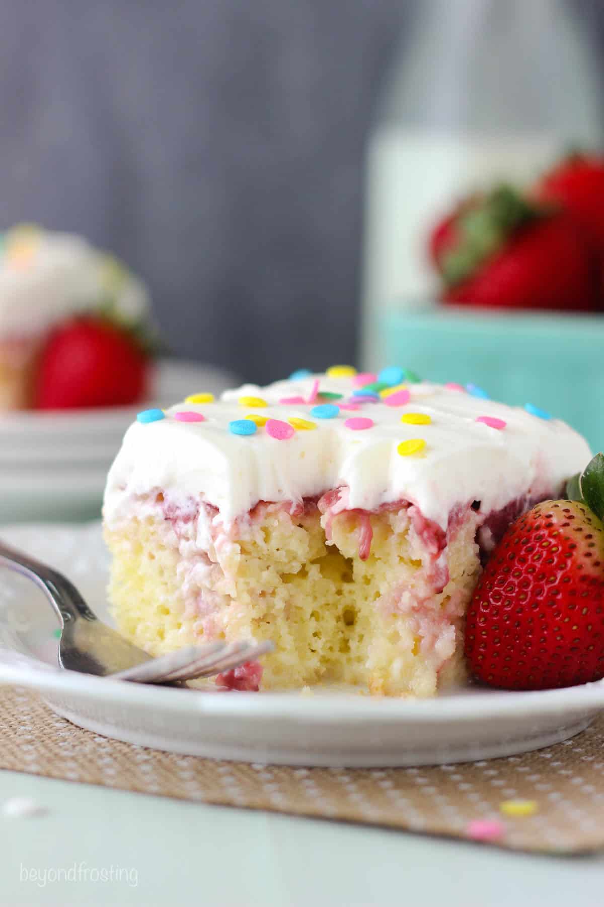 a slice of strawberry cake with a bite taken out on a plate